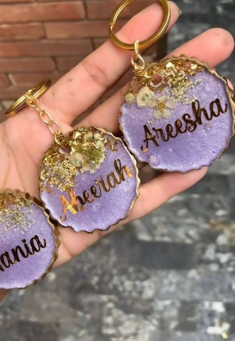 Hand holding personalized purple keychains with names 'Areesha', 'Neha', and 'Mania'.