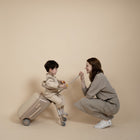 Woman and child playing with a suitcase against a beige background