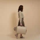 Woman holding a beige suitcase against a beige background