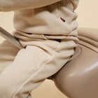 Close-up of beige pants with a small red logo on a beige background