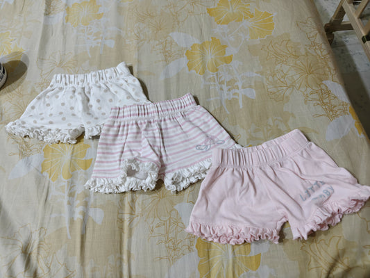 Three pairs of baby bloomers on a floral-patterned bedspread.