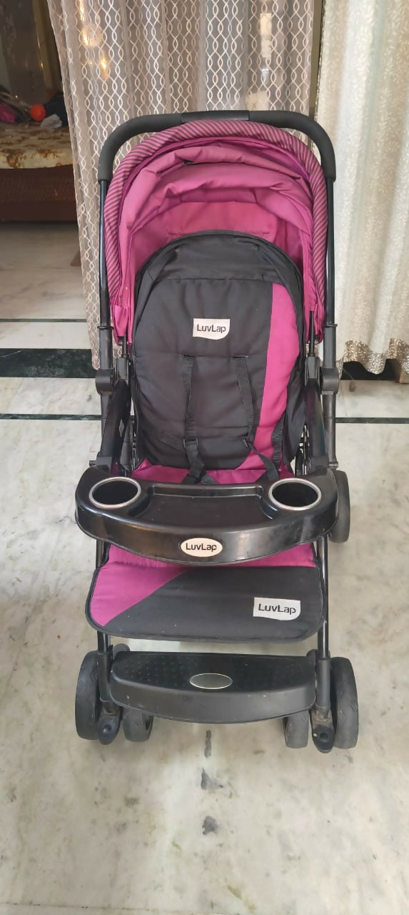 Pink and black stroller on a tiled floor with curtains in the background