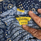 Clothing with a 'globaldes' size label indicating 9-10 years, held by a hand.