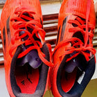 Red athletic shoes with black soles on a wooden surface