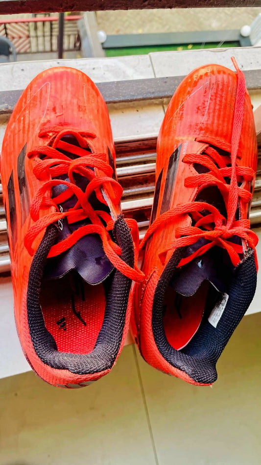Red athletic shoes with black soles on a wooden surface