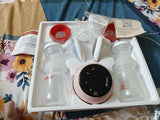 Breast pump set with bottles and control panel in a box on a floral-patterned surface.