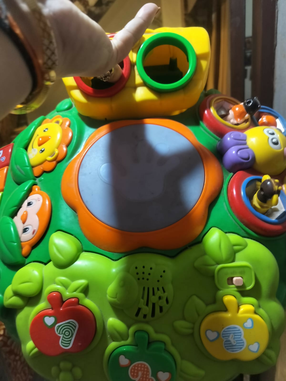Colorful baby activity table with interactive buttons, music features, shape sorter holes, and small toy elements, designed for early learning and play.