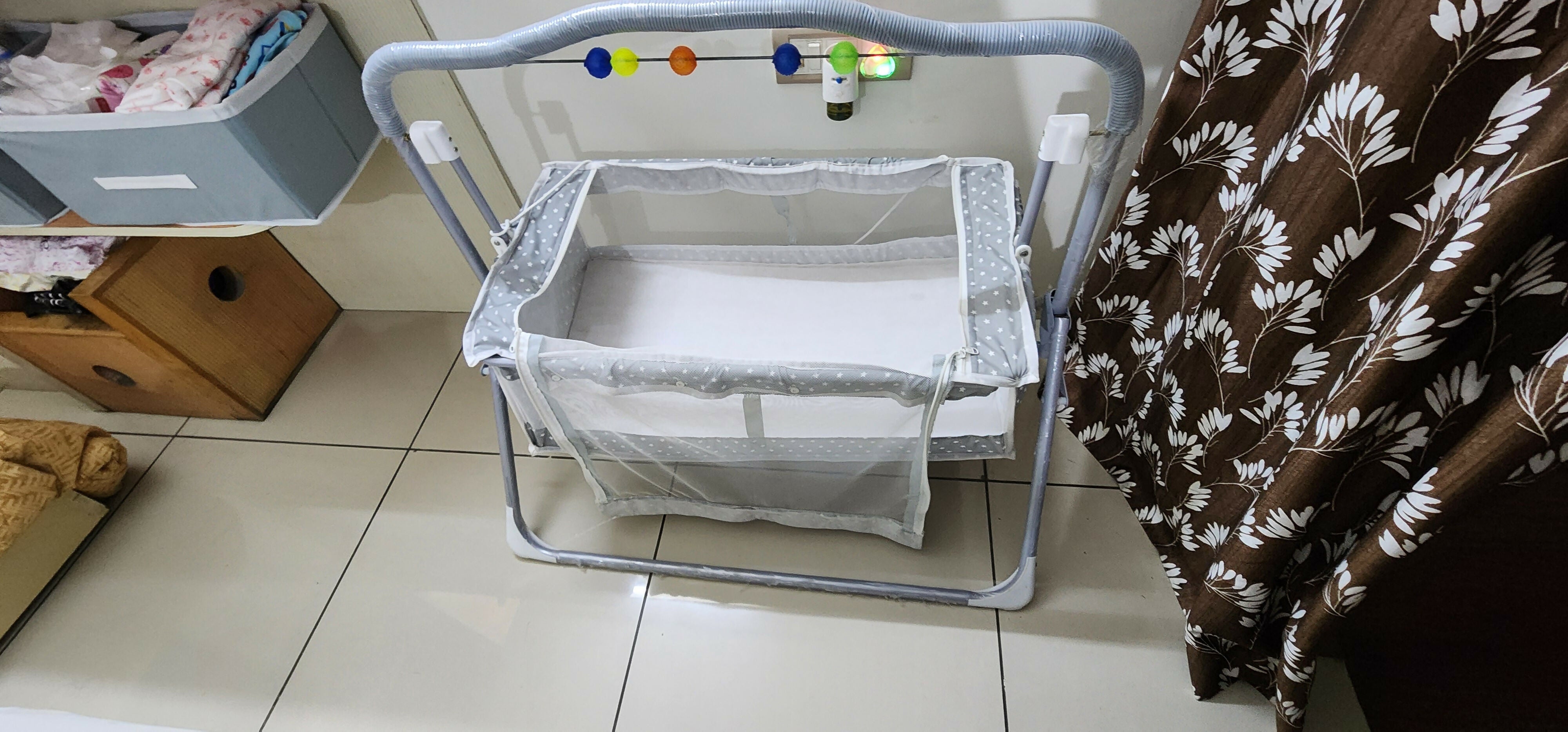 Baby bassinet on a tiled floor with a blanket and storage bins in the background
