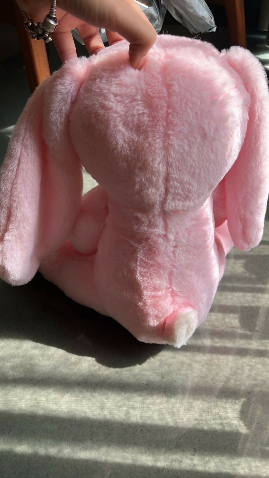 Pink plush toy held by a hand on a textured surface