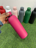 Hand holding a pink water bottle with other colored bottles 