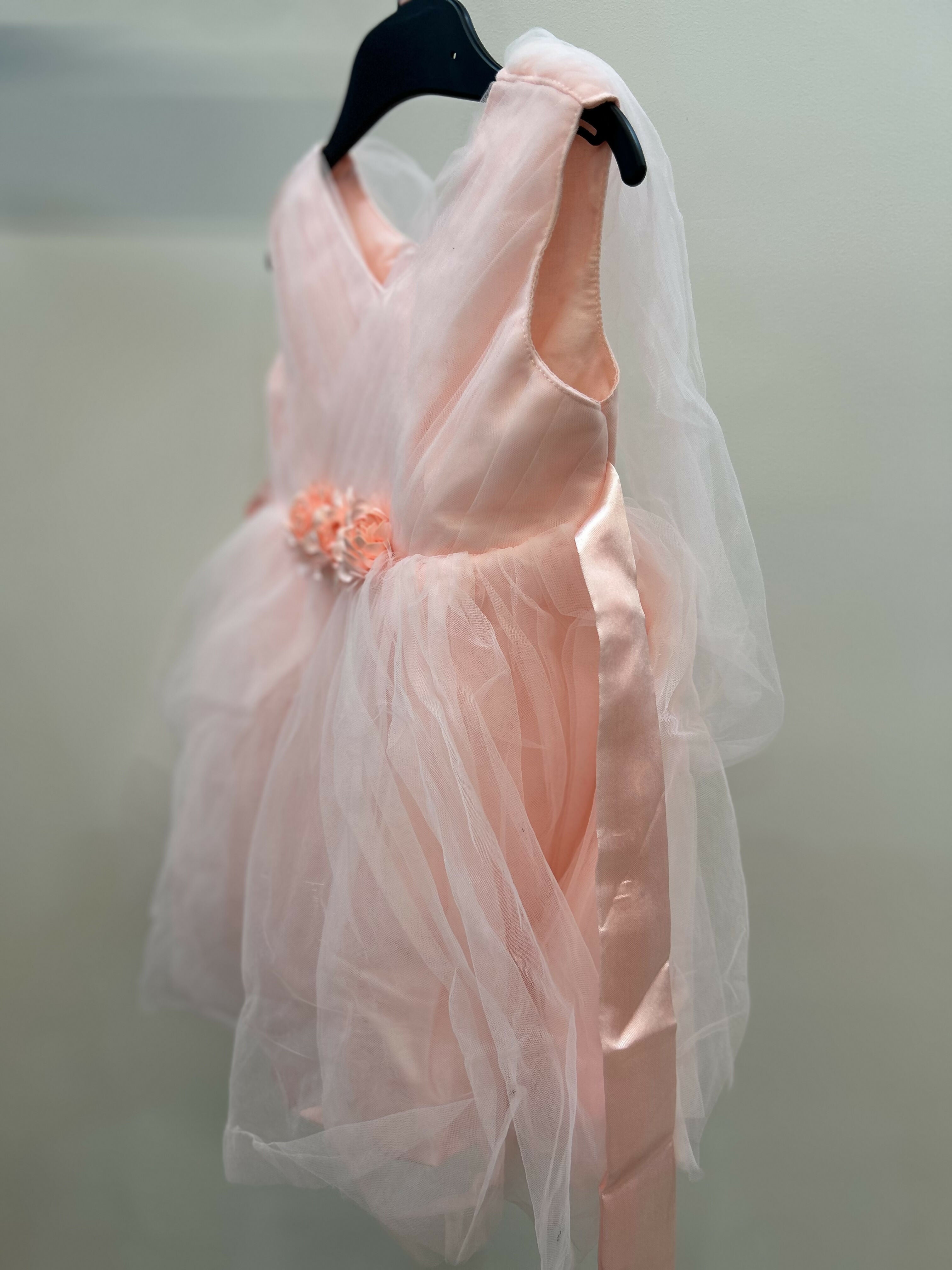 Pink dress with a floral detail on a hanger against a neutral background