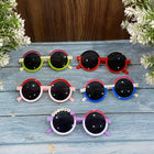 Set of colorful children's sunglasses on a wooden surface with flowers.