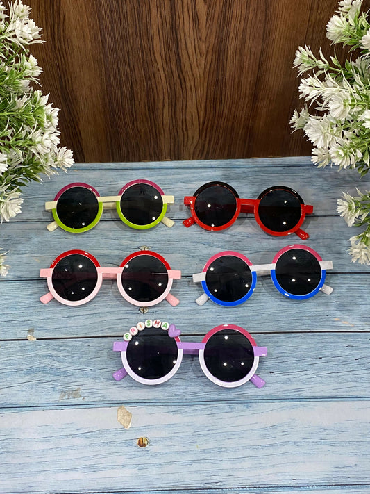 Set of colorful children's sunglasses on a wooden surface with flowers.