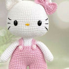 Crocheted toy resembling a character with a pink bow and pink overalls on a light background