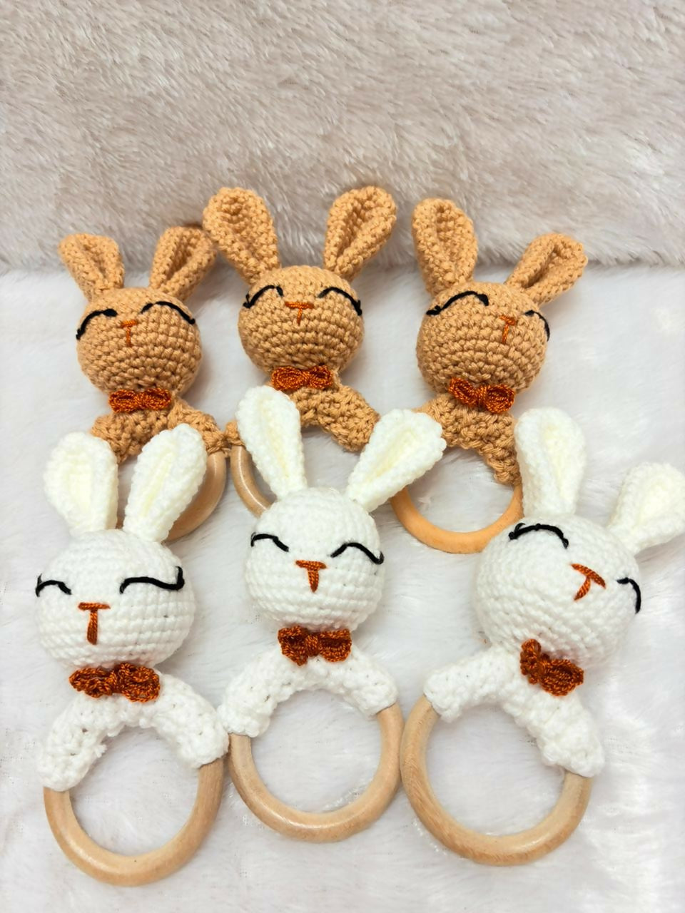 Set of crocheted bunny rattle toys with wooden rings on a soft surface.