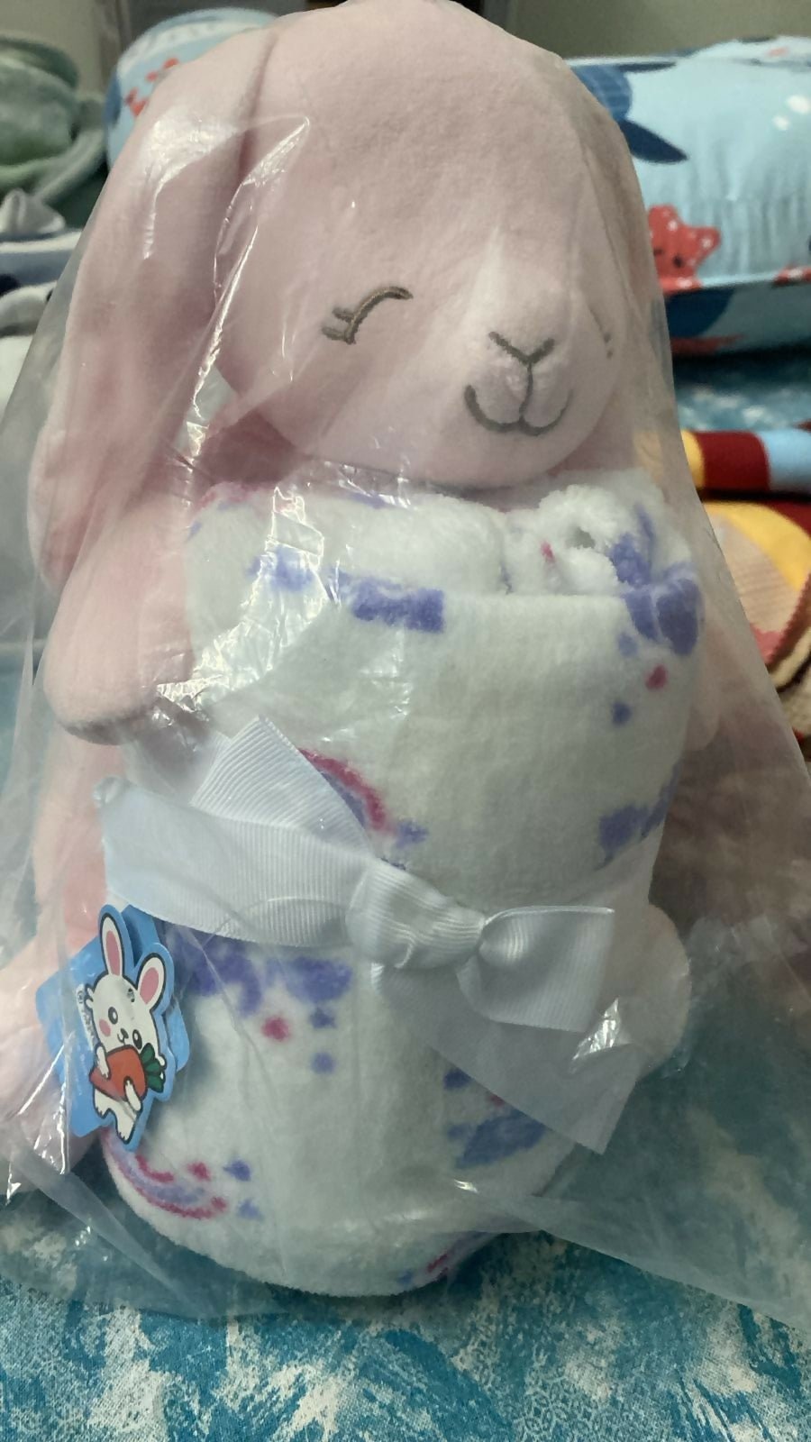 Plush toy with bunny face in clear packaging on a blue blanket