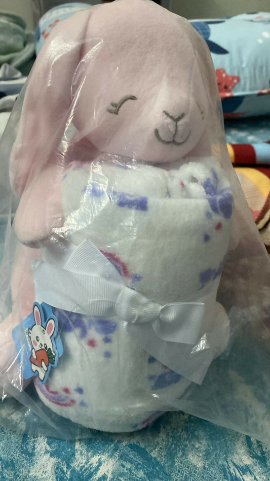Plush toy with bunny face in clear packaging on a blue blanket