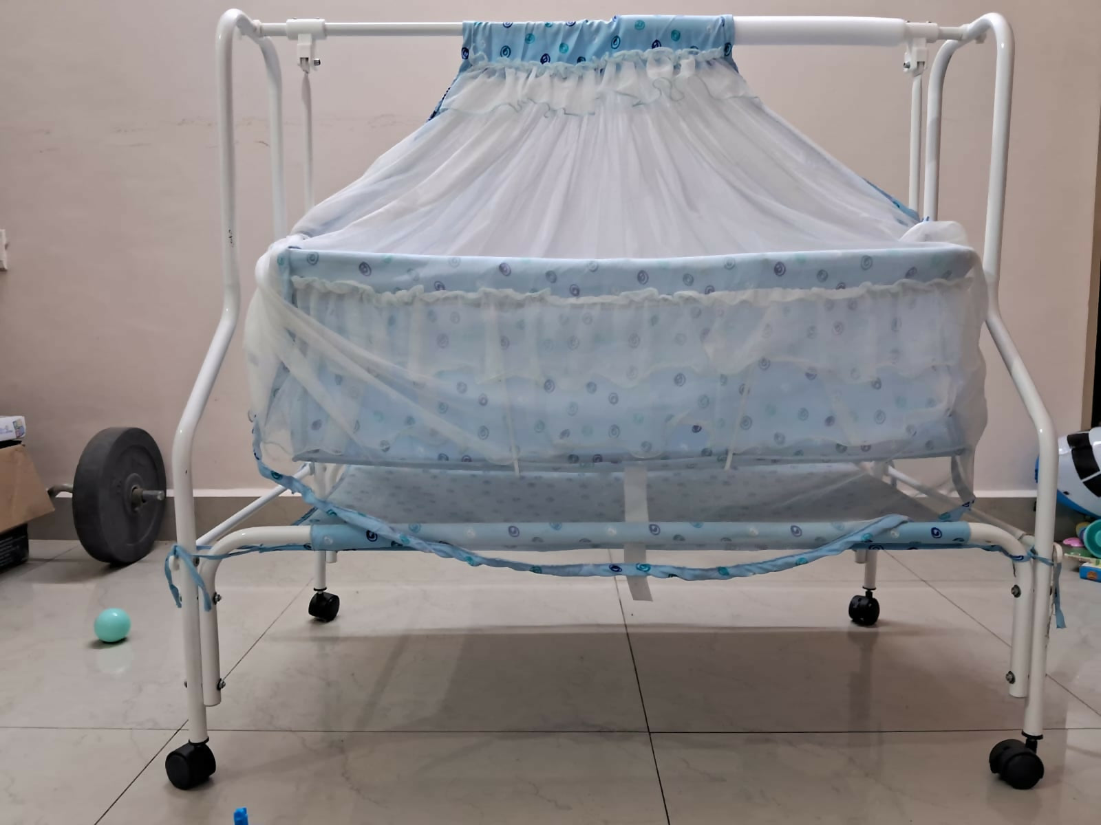 Baby crib with blue bedding on a tiled floor
