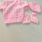 Pink baby sweater, hat, and booties set on a light gray surface
