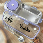 Stainless steel lunch box with purple lid, spoon, and cookies on a wooden surface
