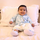 Baby sitting on a bed wearing a patterned outfit.