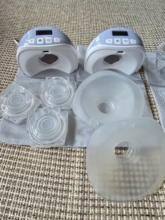 Two breast pumps with additional parts on a textured surface