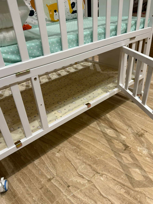 White crib with green and patterned bedding on a wooden floor