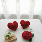 Red heart-shaped and rose-shaped crochet items on a white surface with a 'Handmade with Love' sign.