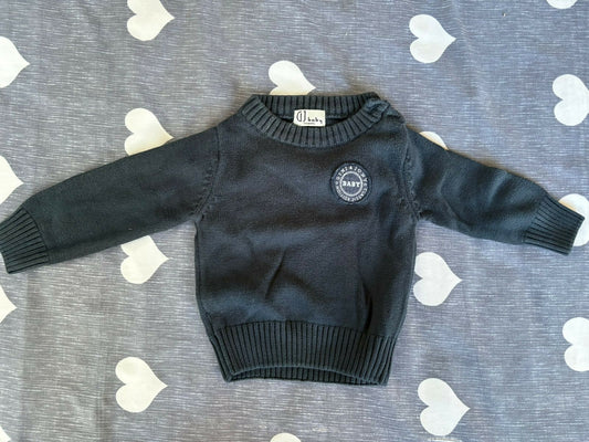 Black sweater with a logo on a gray surface with heart patterns