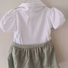 White shirt and green shorts set on a hanger against a plain background