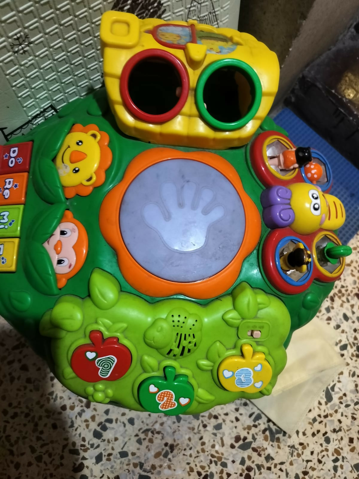 Colorful baby activity table with interactive buttons, music features, shape sorter holes, and small toy elements, designed for early learning and play.