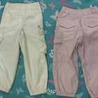 Two pairs of pants, one beige and one pink, on a blue floral-patterned surface.