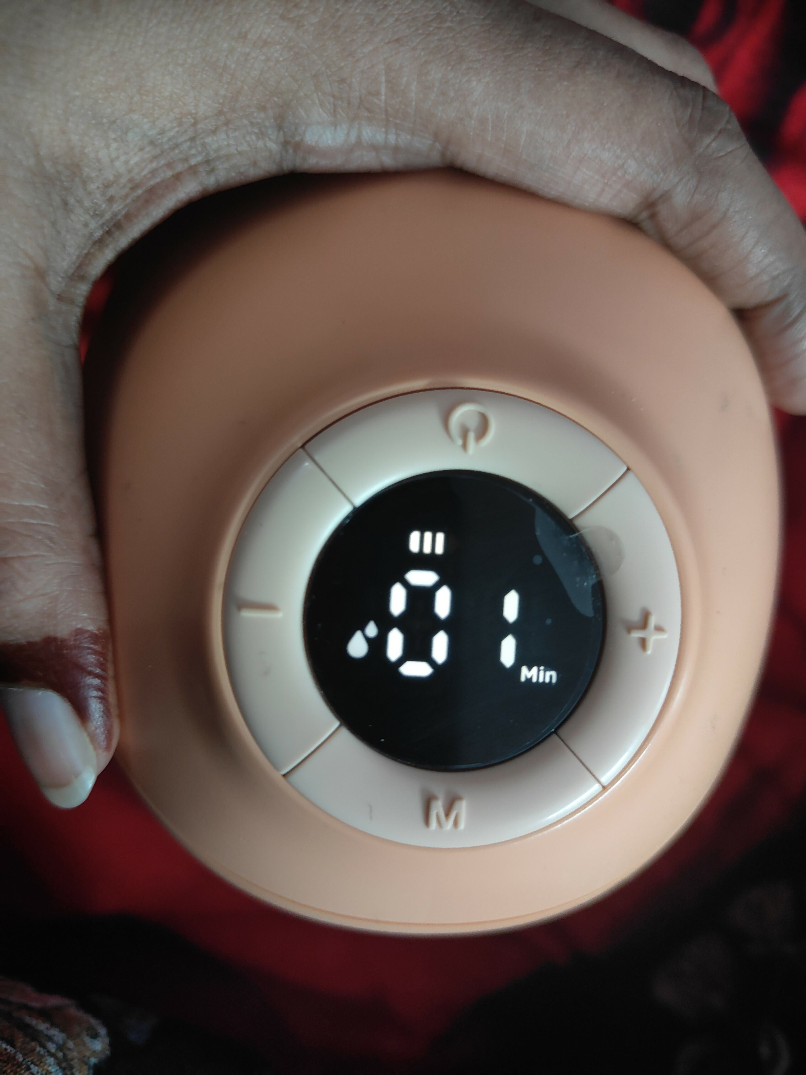 Round electronic device with digital display held by a person wearing gloves.