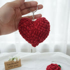 Hand holding a red crocheted heart keychain with a white background