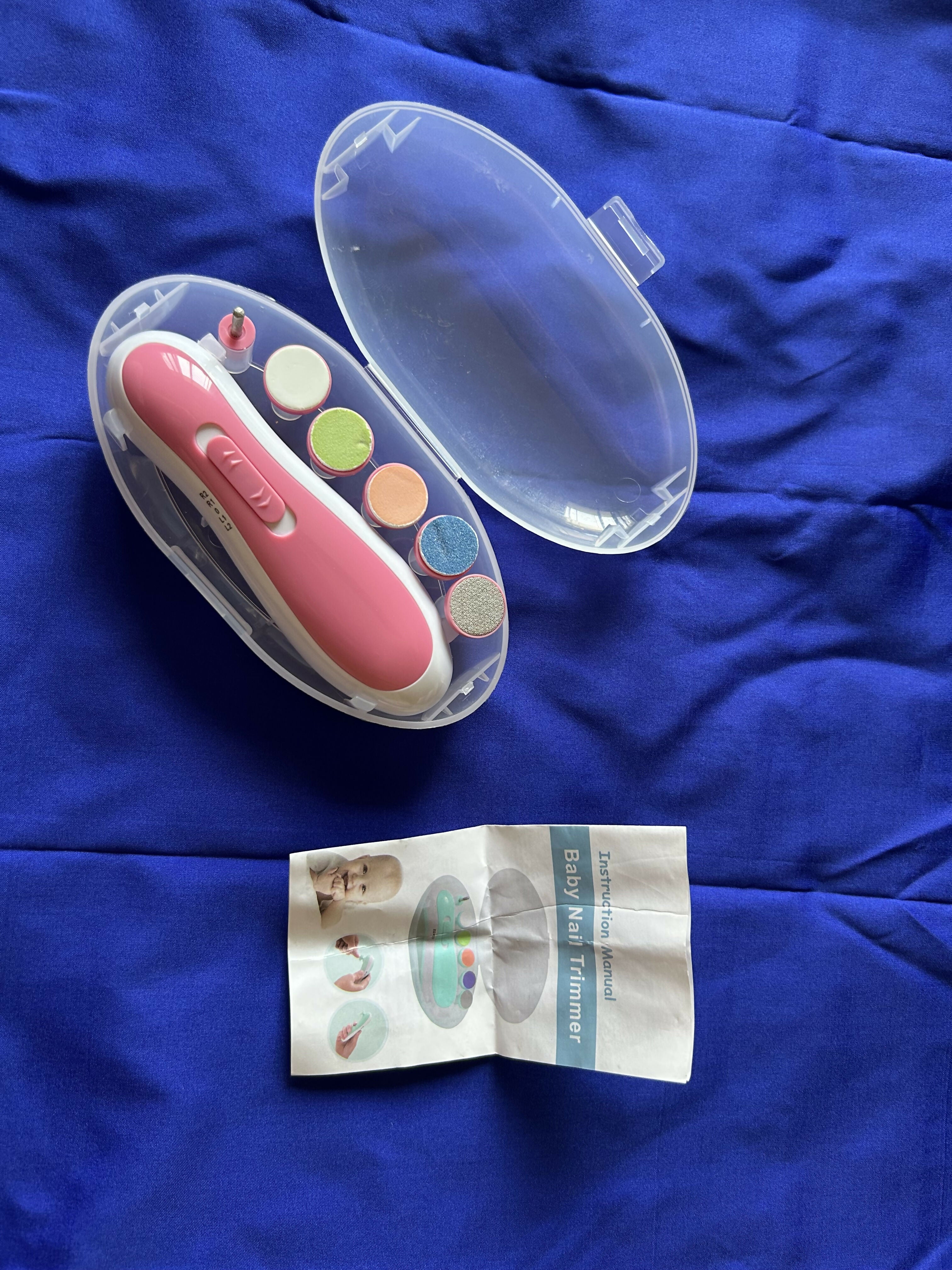 Pink nail clipper with colorful nail pads and instruction sheet on a blue fabric background