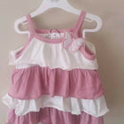 Pink and white baby dress on a hanger against a plain background