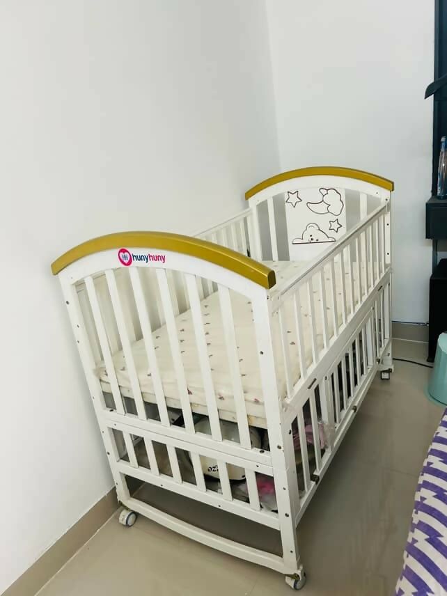 Shop Huny Huny Convertible Baby Cot – Wooden crib with storage, teething rails, wheels, and adjustable height.