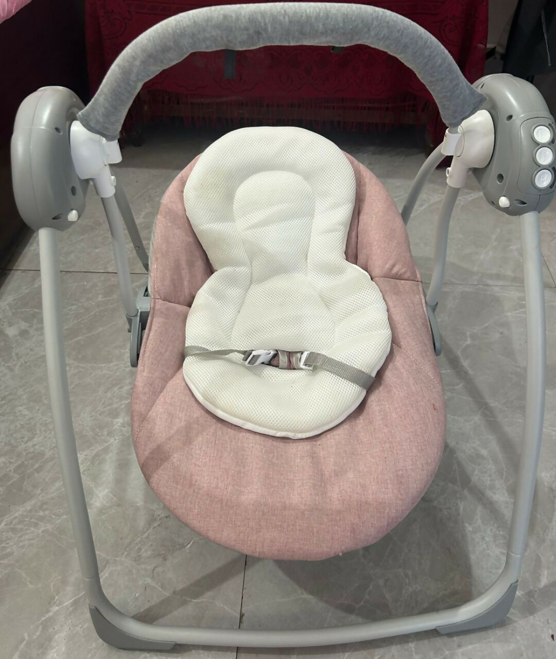 Pink and gray baby swing on a tiled floor