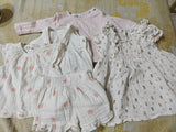 Collection of baby girl's clothing including dresses and a top on a floral-patterned surface.