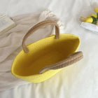 Yellow woven handbag with brown handles on a light background