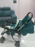 Teal stroller with a patterned seat cover in a living room setting.