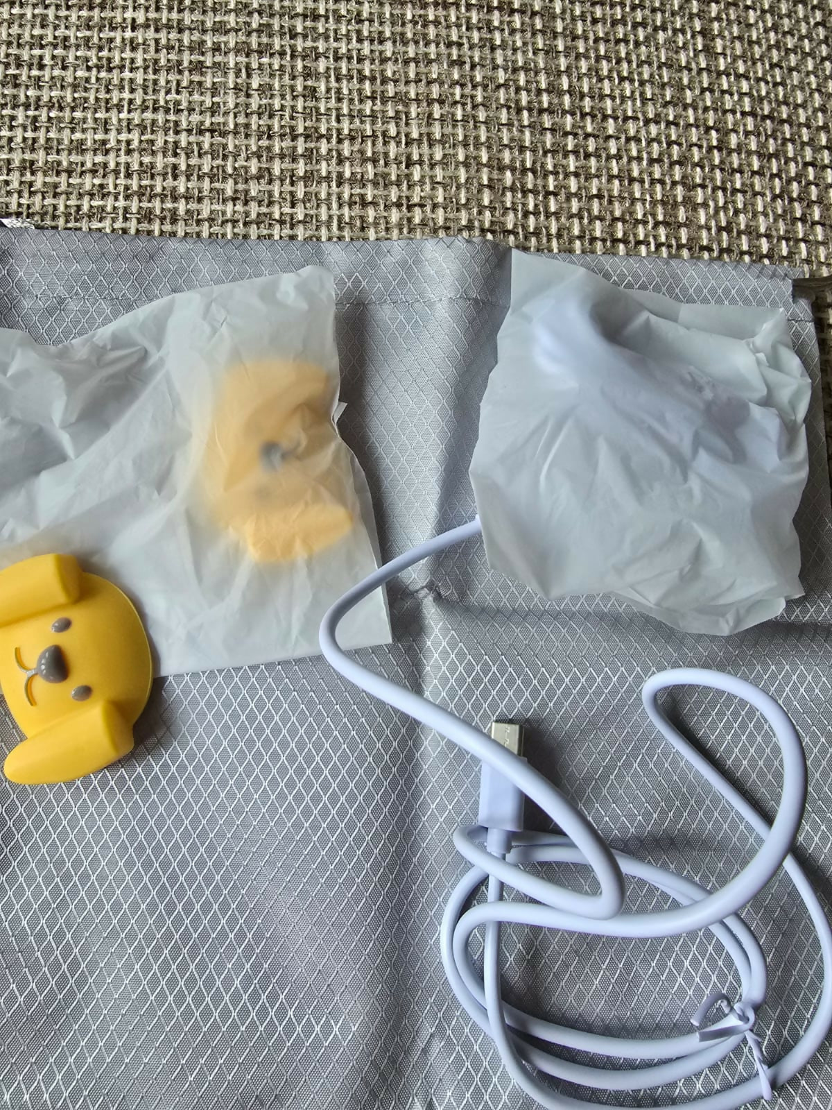Yellow duck-shaped object, white earbuds, and a white cable on a textured surface.