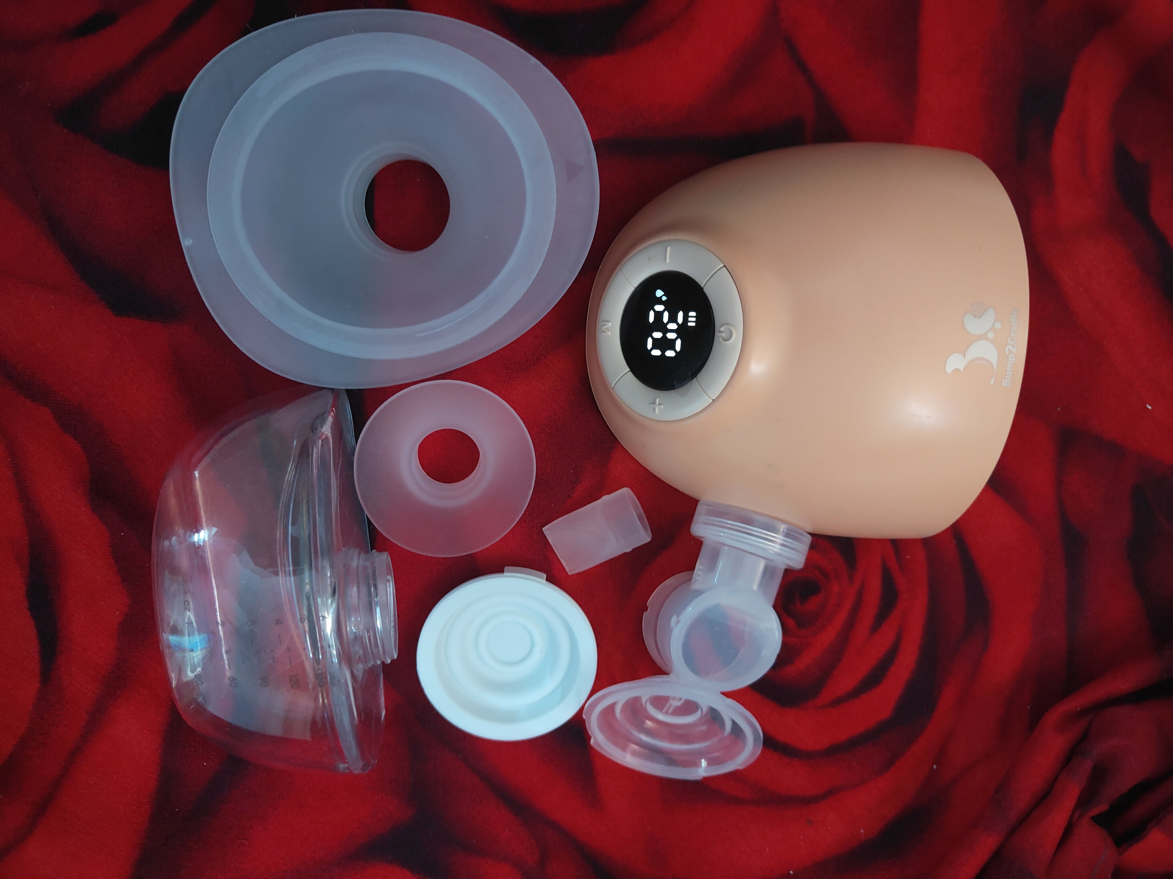 Breast pump with various parts on a red fabric background