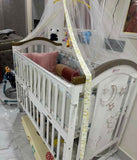 White crib with brown accents and decorative elements in a room setting.