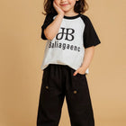 Child wearing a black and white shirt with text and black pants 