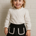 Child wearing a white blouse and black skirt with lace details 