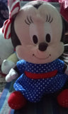 Plush toy resembling a character with a candy cane on top of its head, wearing a blue outfit with white polka dots and a red belt.