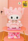 Pink cartoon plush toy with a bow on a pink stool against a pink wall with 'Happy Kado' branding.