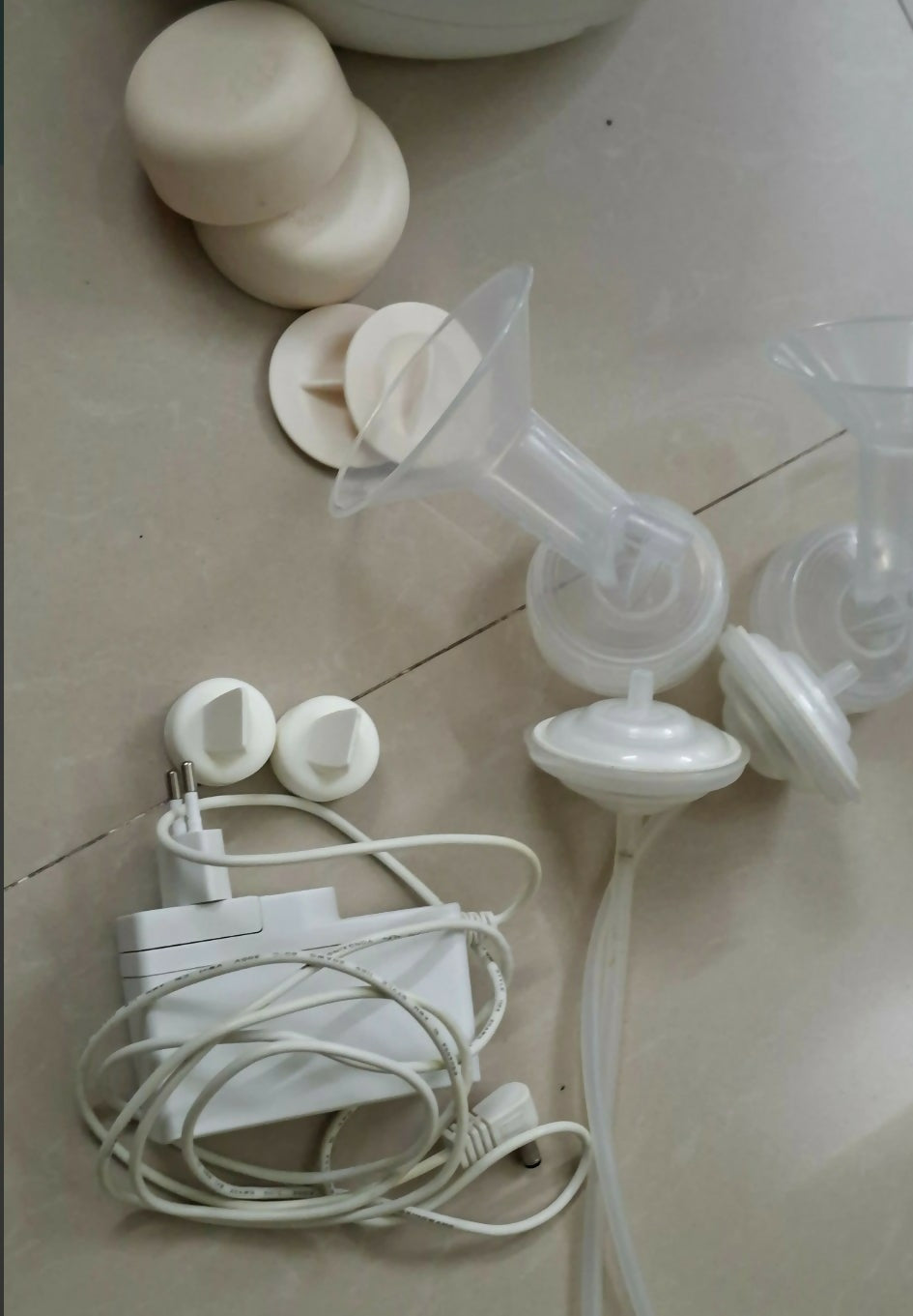 Breast pump parts on a tiled floor with power adapter and cable.