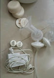 Breast pump parts on a tiled floor with power adapter and cable.